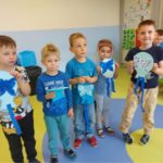 Na zdjęciu widać dzieci z grupy Skrzaty. Chłopcy stoją obok siebie, ubrane mają koszulki w kolorze niebieskim. W rękach trzymają wykonane przez siebie niebieskie balony z motylami.